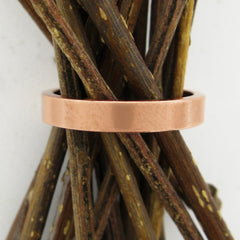 Front view of flat copper band ring around a bunch of dark wood twigs with white background