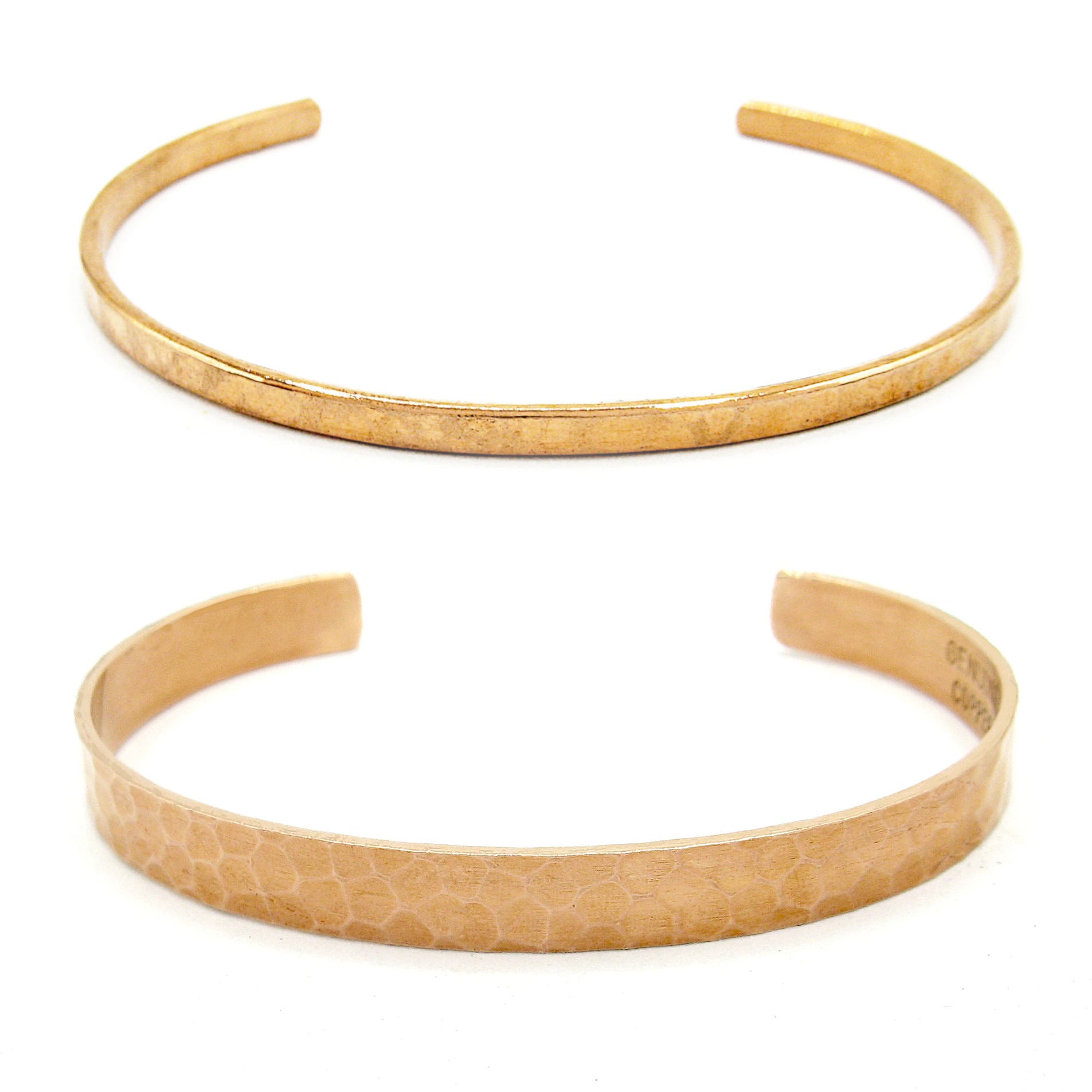 Front view of both a gently hammered narrow copper open-cuff bracelet above and a gently hammered wide copper open-cuff bracelet on a white background