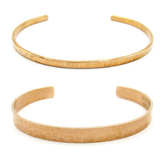 Front view of both a gently hammered narrow copper open-cuff bracelet above and a gently hammered wide copper open-cuff bracelet on a white background