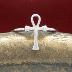 Front view of a silver ring in the shape of an Egyptian ankh symbol resting on a rounded textured golden ceramic prop with a dark red background.