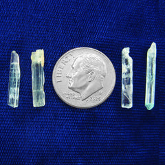 4 long narrow Nigerian emerald crystals lined up next to dime to show scale on dark background