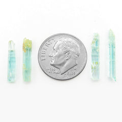 4 long narrow Nigerian emerald crystals lined up next to dime to show scale on white background