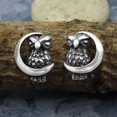 Silver owl and crescent moon earrings on a tree branch.