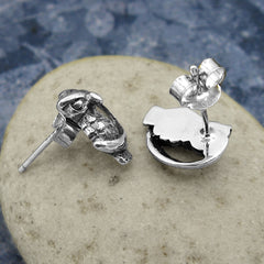 Side view of silver owl and crescent moon earrings on a stone.