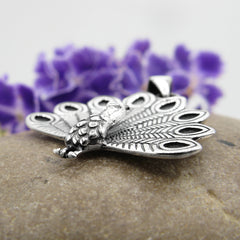 Side view of three-dimensional sterling silver bird jewelry pendant with detailed feathers fanned out open oxidized finish.