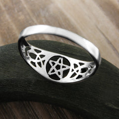 Back/inside view from slightly above of cut-out sterling silver Celtic style ring with pentagram and elongated triquetra knot resting on dark wooden rounded prop with tan wood in background.