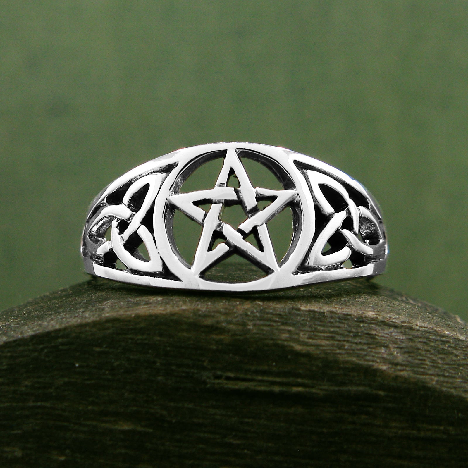 Front view of cut-out sterling silver Celtic style ring with pentagram resting on dark wooden rounded prop with dark green background.