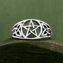 Front view of cut-out sterling silver Celtic style ring with pentagram resting on dark wooden rounded prop with dark green background.