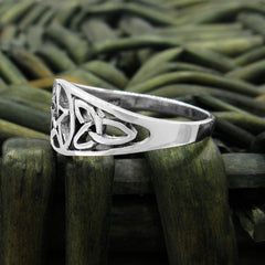 Side view of cut-out sterling silver Celtic style ring with elongated triquetra knot resting on dark green coarse woven basket with blurry background.