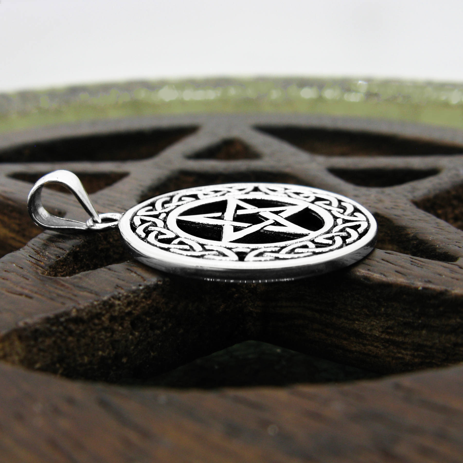Side view of silver pentacle necklace with knotwork frame on wooden background