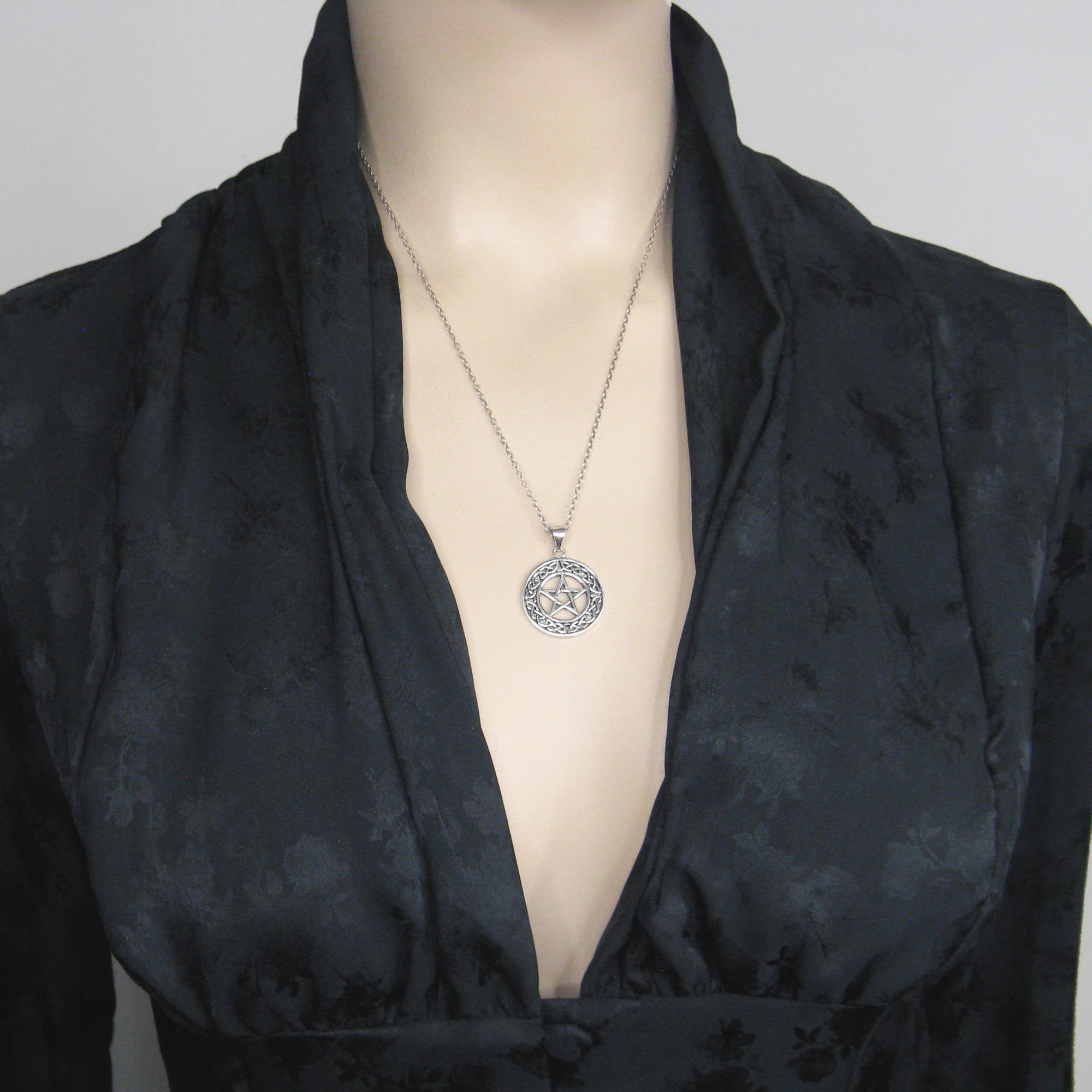Mannequin wearing a black garment with a silver pentagram pendant.