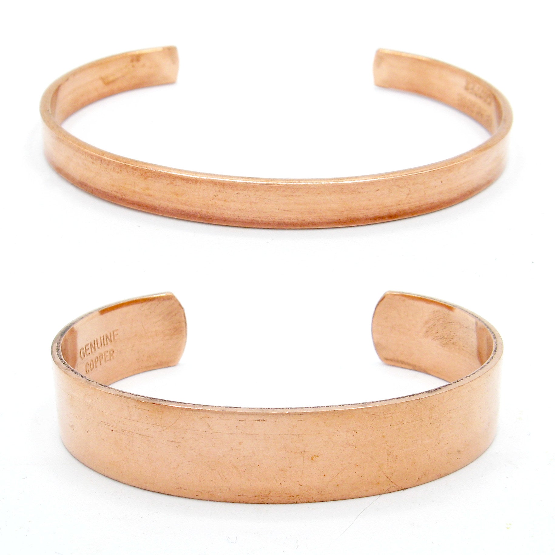 Front view of two plain polished copper open cuff bracelets, one narrow (above), one wide (below), on white background