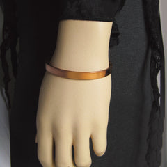 Close up view of a narrow plain polished copper cuff bracelet worn on the hand of a mannequin dressed in black and dark clothes against grey background