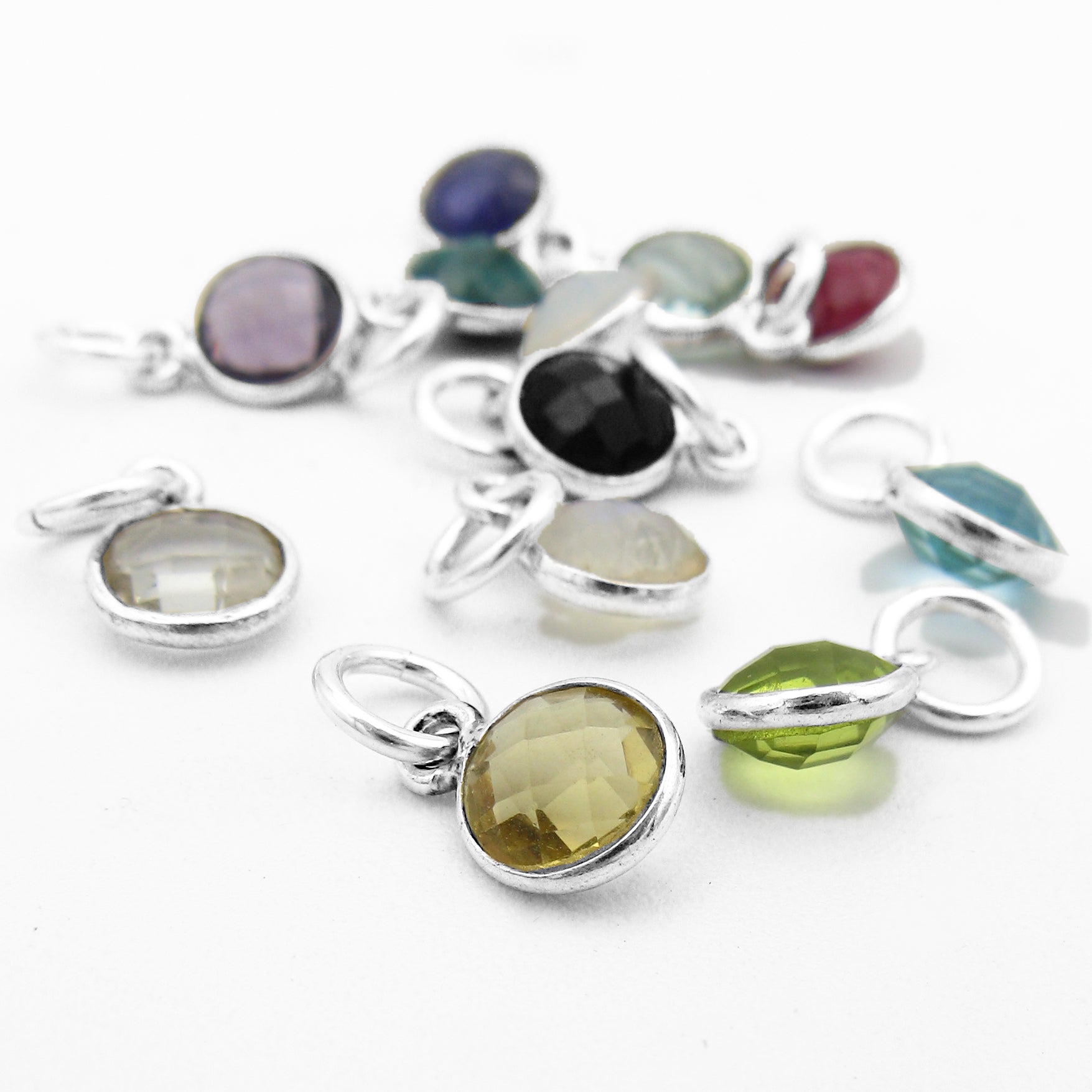 Close-up photo of random arrangement of multicolored faceted birthstone charms in silver settings against white background.