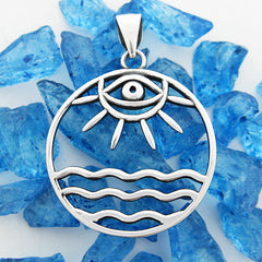 Front view of round cutout silver pendant with eye/sun/ocean design on random pieces of blue glass on white background