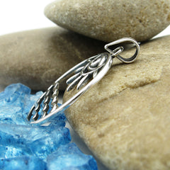 Side view of round cutout silver pendant with eye/sun/ocean design leaning against smooth stones on random pieces of blue glass on white background