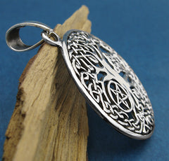 Side view of cut-out Tree of Life pendant on wood branch with green background.