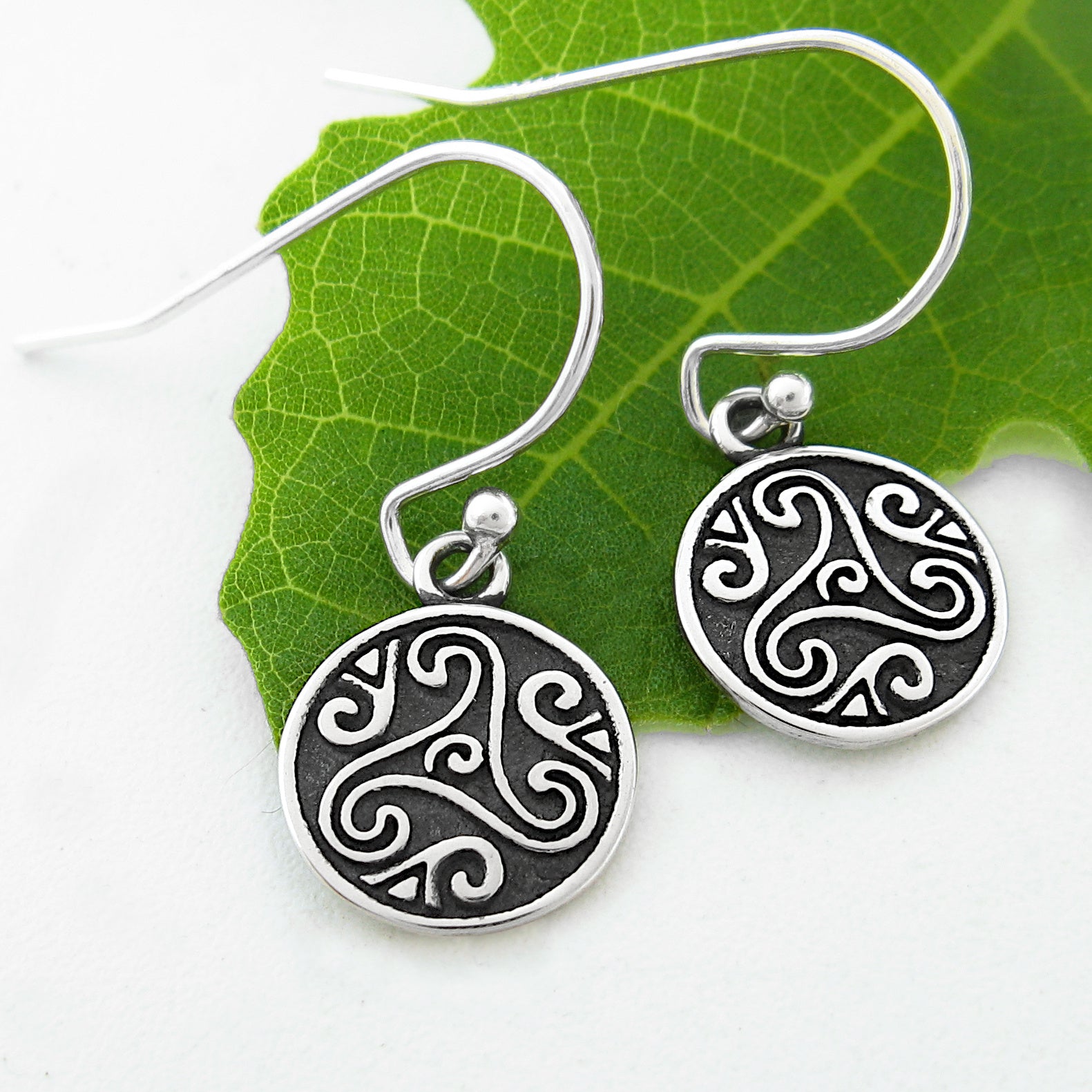 Silver earrings with intricate Celtic designs on a green leaf background