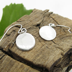 View of opposite side of silver round Celtic earrings on a piece of wood with a green leaf background