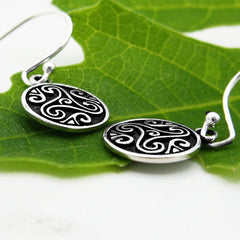 Side view of silver earrings with intricate Celtic designs on a green leaf