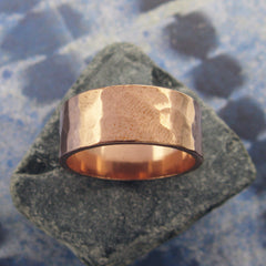 Gently hammered pure copper band ring resting on trapezoidal shaped grey stone with background of blue and white pattern.