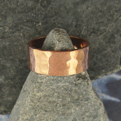 Gently hammered pure copper band ring displayed on triangular shaped grey stone with background of grey stone and blue pattern.