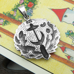 View of backside of a round oxidized silver pendant with witch's broom and hat and crescent moon surrounded by flowers and stars and overall hammered finish resting on a yellow Tarot card with a wooden prop in the background
