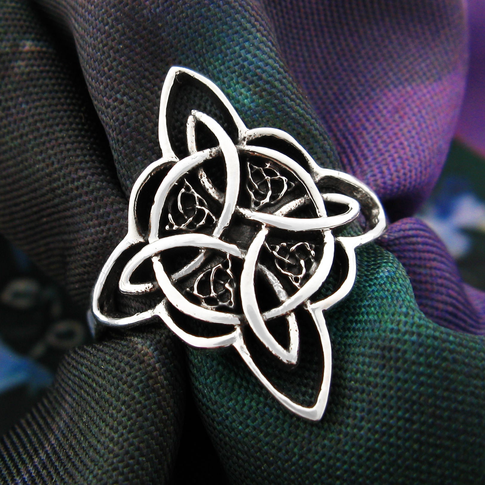 Fancy silver Witch's Knot ring on dark colorful cloth background