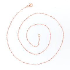 A delicate copper chain necklace coiled in a spiral on a clean white background, featuring a lobster clasp and an adjustable ring extender.