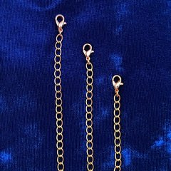 Three copper chain extender links with lobster clasps, displayed vertically against a textured blue velvet background.