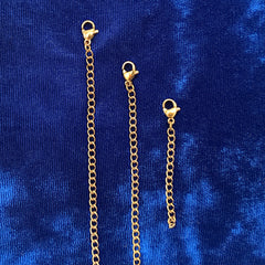 Three gold chain extender links with lobster clasp ends, displayed vertically on a textured blue velvet background.