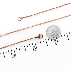 A copper chain necklace with a lobster clasp and extender loop, shown alongside a US dime coin and a black ruler scale on a white background to indicate size.