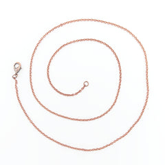 A delicate copper chain necklace with a lobster clasp, arranged in a neat spiral on a plain white background.