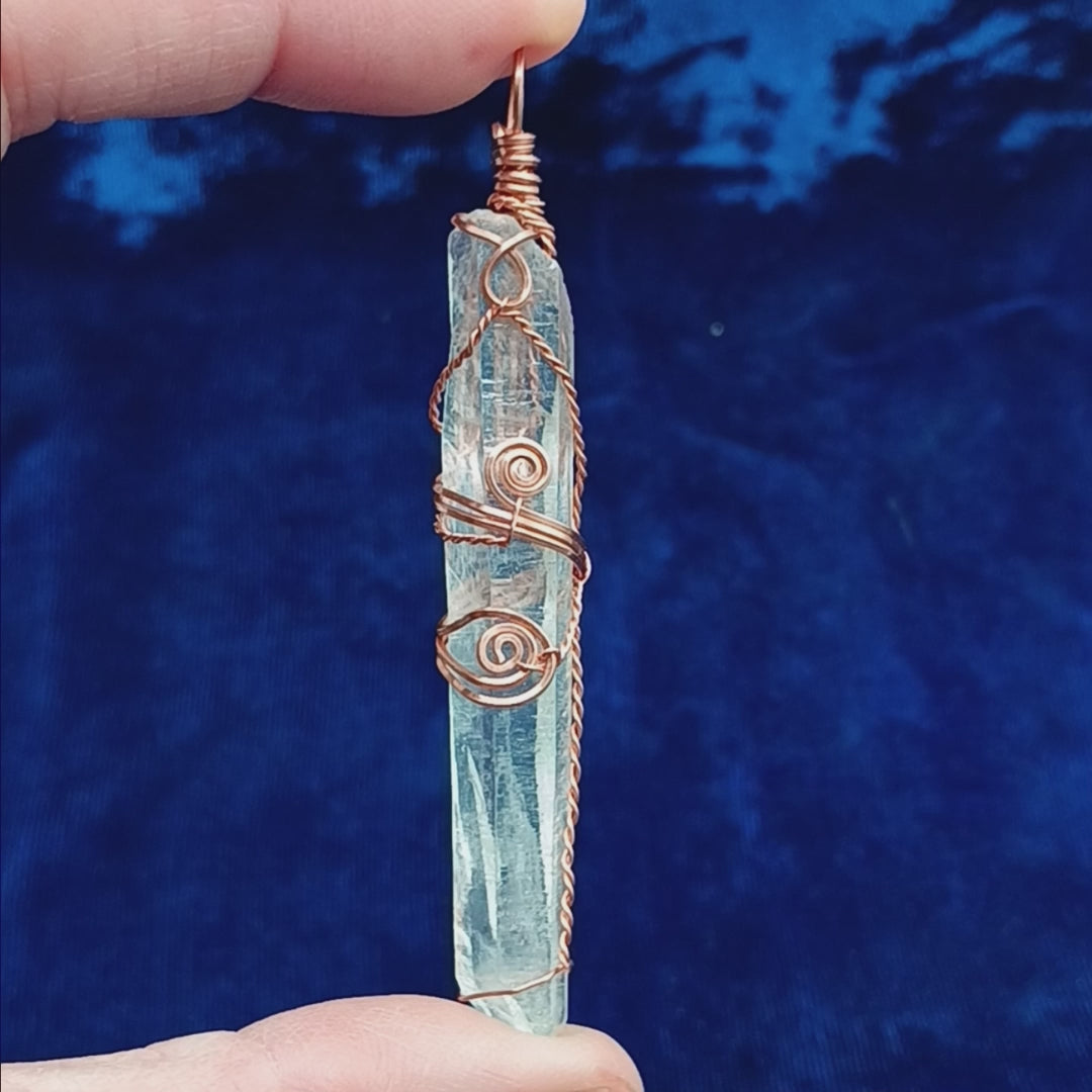 long clear copper wire wrapped quartz crystal with spiral designs against a dark blue background
