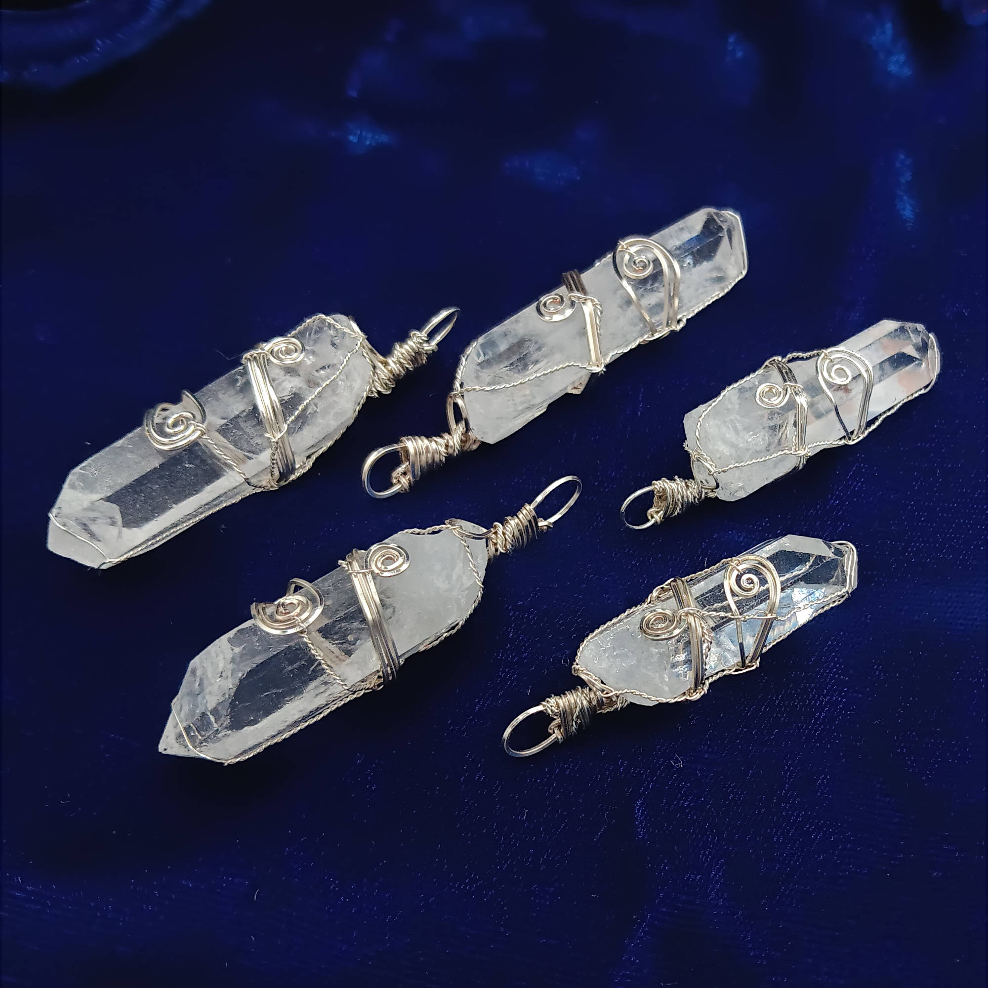 Raw Quartz Crystal Point Pendant – Silver-Plated Wire Wrapped Necklace, various pendants, laying on blue background