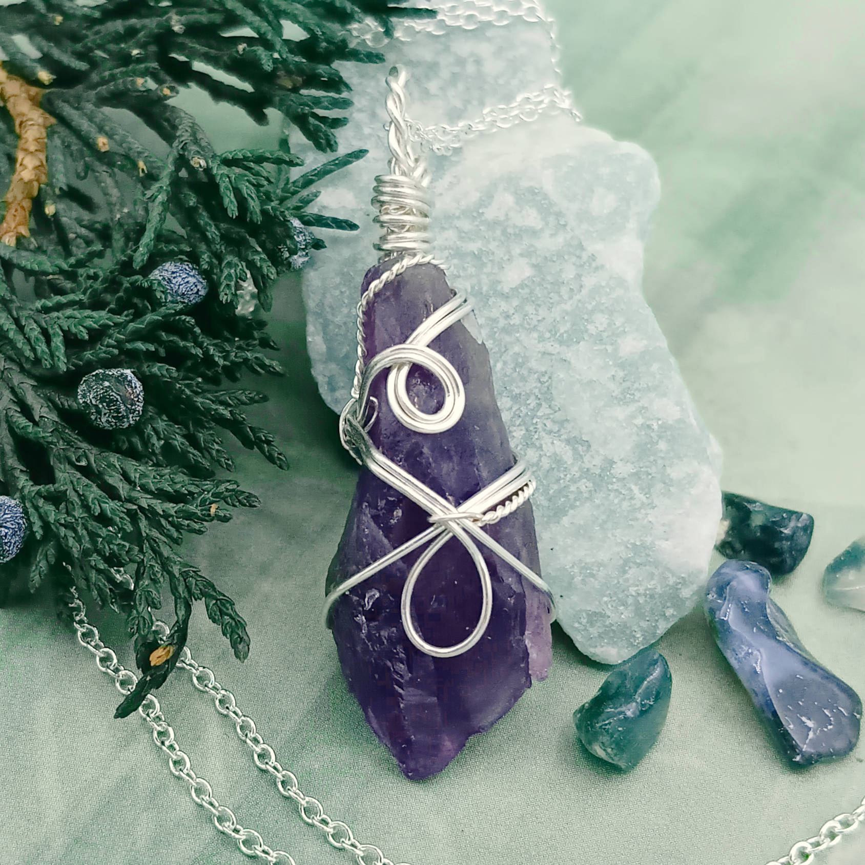 Raw Amethyst Crystal Point Pendant silver wire wrapped on green background with plants and pebbles