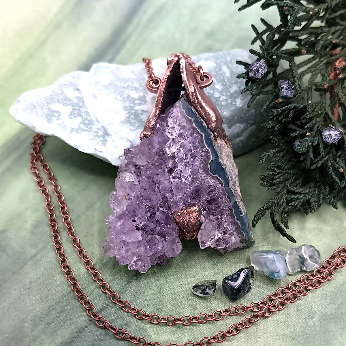 Raw triangle amethyst stalactite copper electroformed pendant with green stone, plants, and tiny pebbles on green background