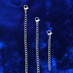 Three stainless steel chain extender links with lobster clasp ends, displayed vertically against a textured royal blue velvet background.