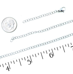 A stainless steel chain extension strap with a lobster clasp, shown on a white background alongside a coin for scale and a ruler with inch markings to indicate length.