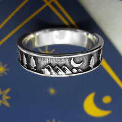 Oxidized sterling silver band type ring with trees, mountains and moon design displayed on a dark blue card with gold moon graphics on a white background.
