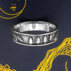 Oxidized sterling silver band type ring with trees and mountains design displayed on a dark blue Tarot card with gold graphics.