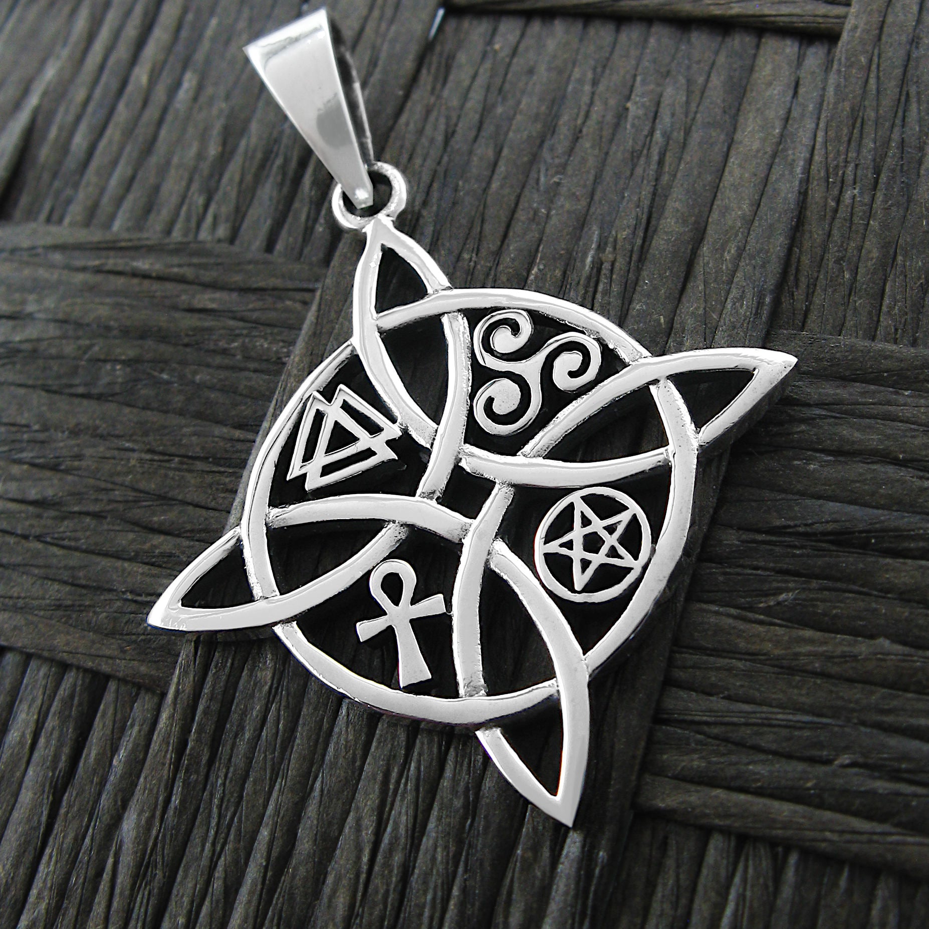 Front view of a silver witch's knot pendant with four symbols on a dark basket weave background