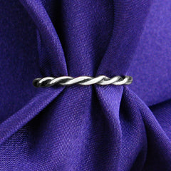 Slender silver ring with a braided rope pattern design displayed on a ruched purple cloth.