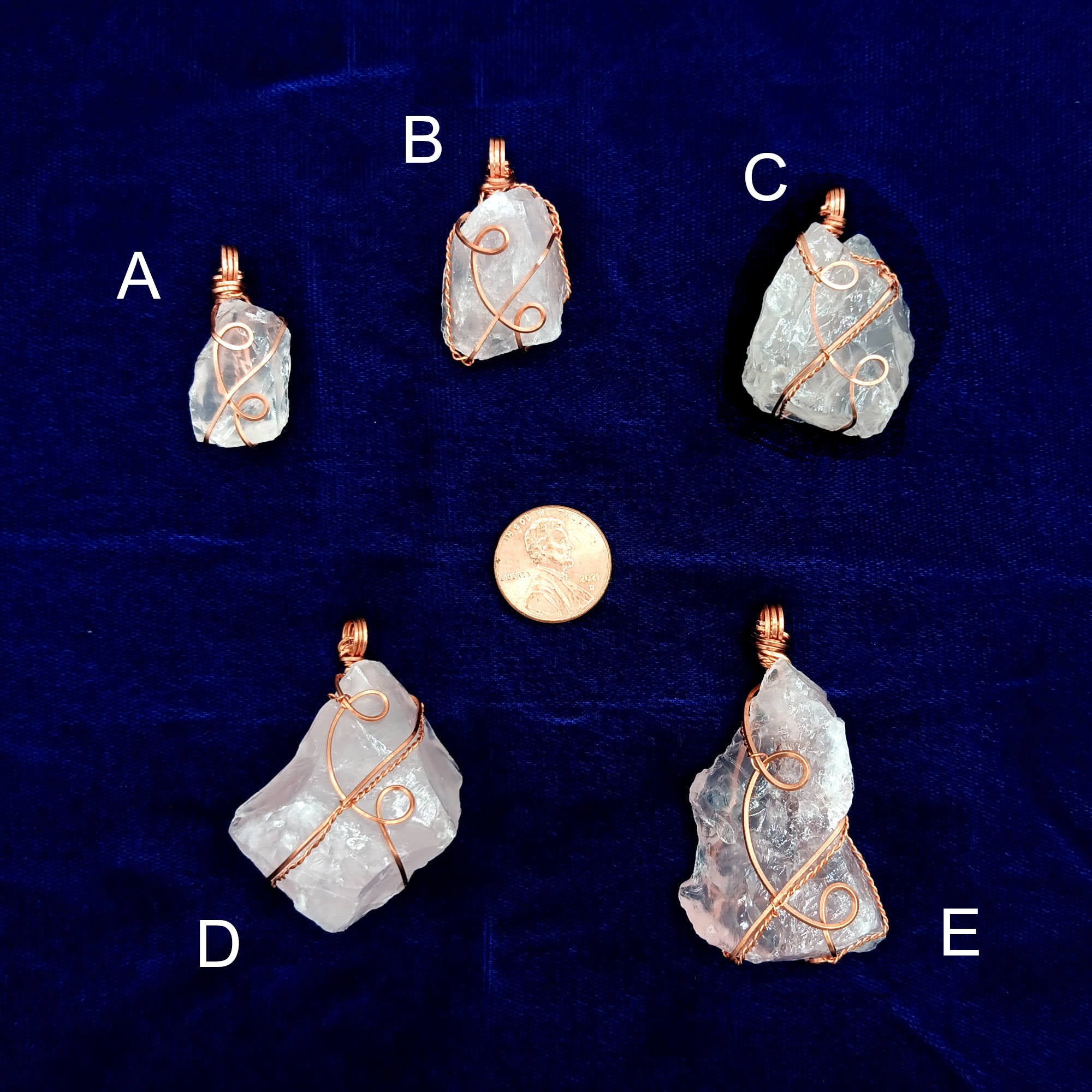 Five rose quartz crystal pendants labeled A to E on a dark blue background with a penny for scale.