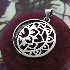 View of back side of round cut-out silver pendant with crescent moon and lotus design on maroon candle with greenish background