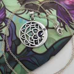 Round cut-out silver pendant with crescent moon and lotus design and chain on round purple and green flowery background with white