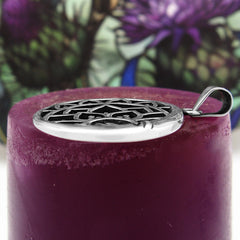 Side view of round silver pendant on maroon candle with purple and green flowery background