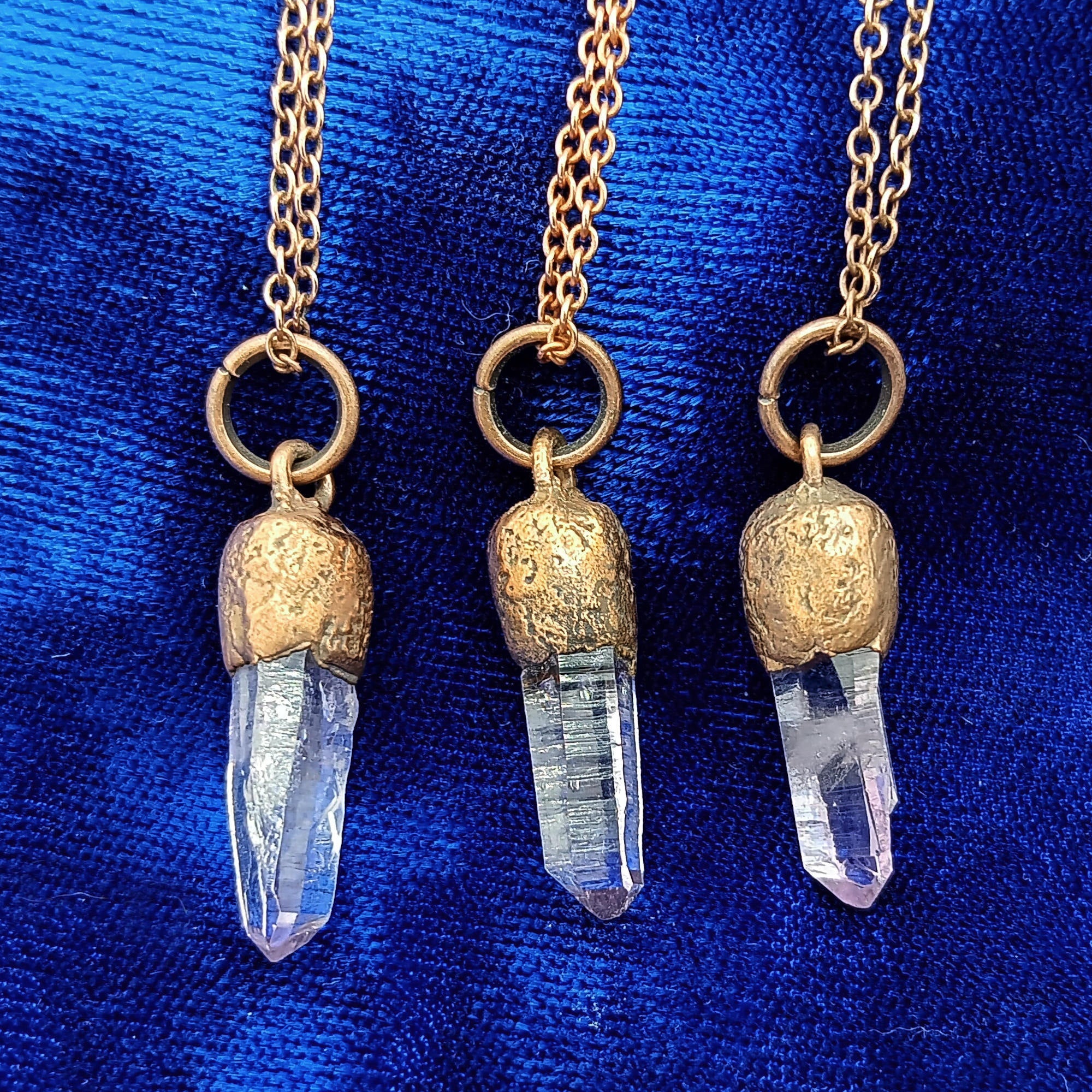 Three copper crystal point necklaces with veracruz amethyst and textured copper caps, displayed against a rich blue fabric background.