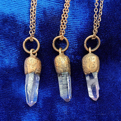 Three copper crystal point necklaces with veracruz amethyst and textured copper caps, displayed against a rich blue fabric background.