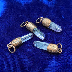 Three veracruz amethyst crystal point pendants with textured copper caps and loops, resting on a deep blue velvet fabric background.